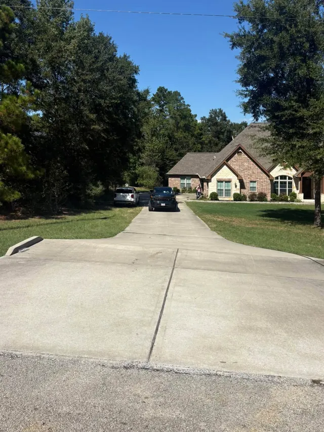 Long concrete driveway leading to a brick and stone house before cleaning